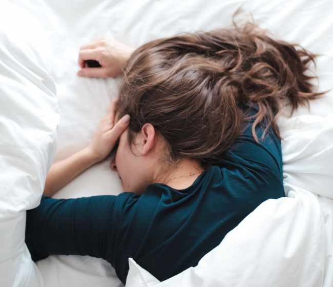 woman in blue shirt laying in bed covering her head with her hand