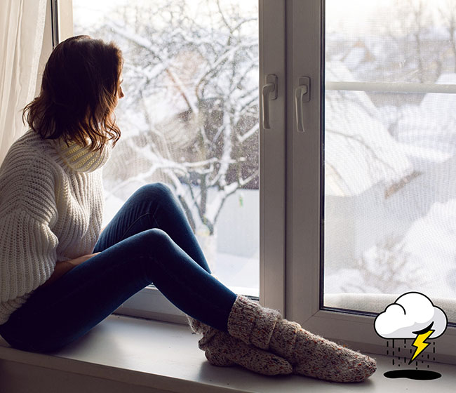 A young woman suffering from anxiety and depression looking out the window during winter
