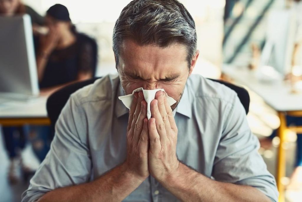 Man in blue shirt blowing nose after sneezing