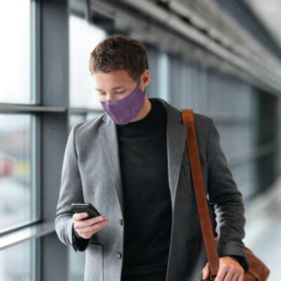 a man at the airport looking at his phone and wearing a mask