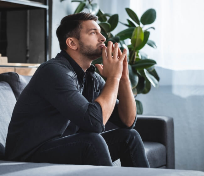 A young man thinking and putting his hands together while waiting to talk to a psychologist online