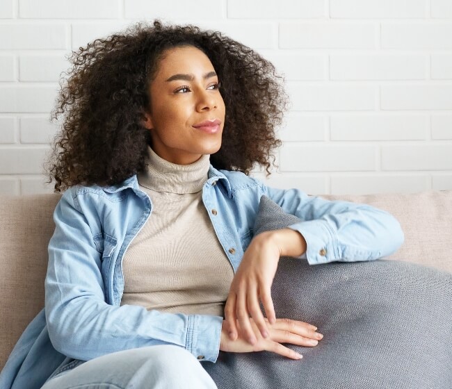 WomensHealthSpecialty_Hero A young woman sitting on a coach waiting to talk with a gynecologist online