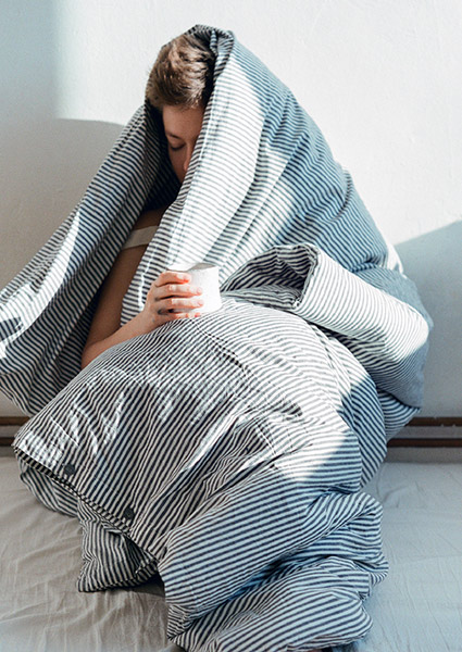 a sick woman drinking tea under a blanket waiting to get an online doctor’s note