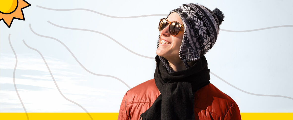 Person wearing sunglasses and a winter hat soaking up the sun to get vitamin D in winter. An illustrated sun with rays is in the top left corner.