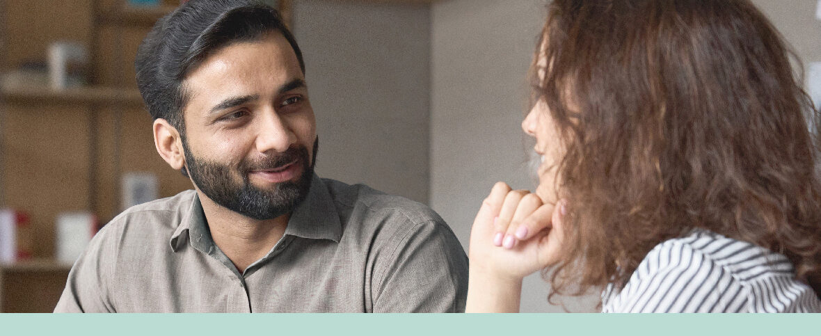 A male and female coworker sitting across from each other smiling, representing employee mental health.