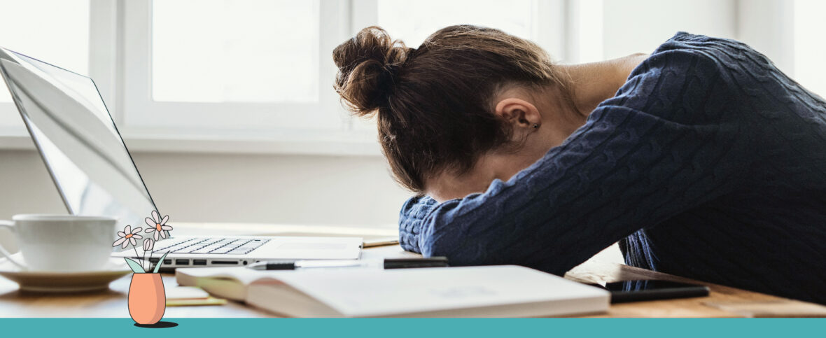 Woman experiencing winter blues with her head down on her desk in front of a laptop. Below are illustrated flowers in a vase.