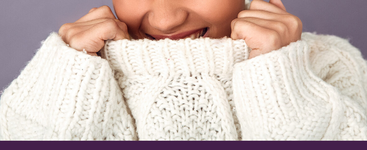 Woman with winter skin problems pulling her white knit sweater up towards her chin.