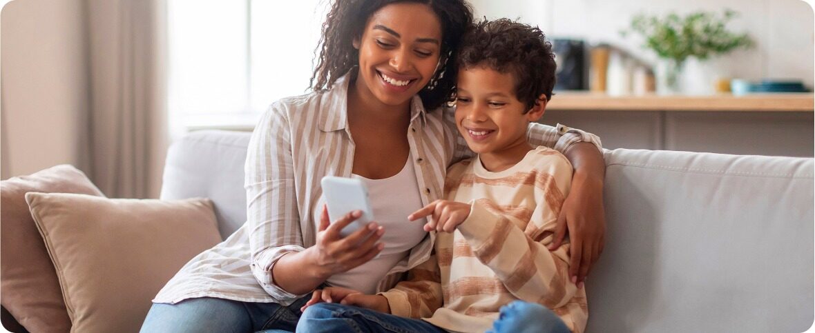 mother and child sitting on a grey couch looking at a phone